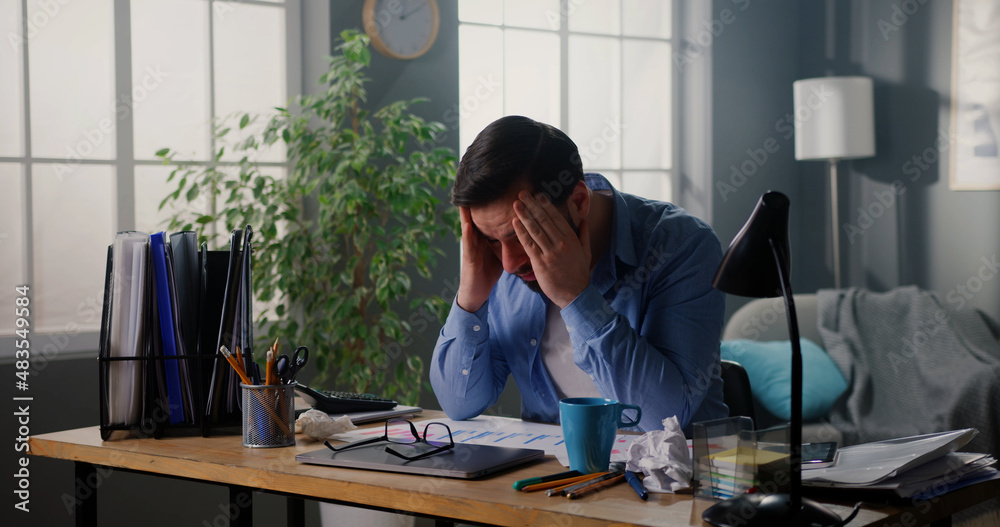 Young tired man working at home office, looking very tired, suffering from splitting headache. Exhausted manager sitting at workplace, trying to cope with anxiety. Young tired man working at home office, looking very tired, suffering from splitting headache. Exhausted manager sitting at workplace, trying to cope with anxiety.