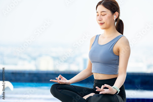 Beautiful asian woman doing a yoga exercise on he rooftop of a skyscraper at sunset.Yoga and meditation in a modern urbanistic city. Young attractive girl .