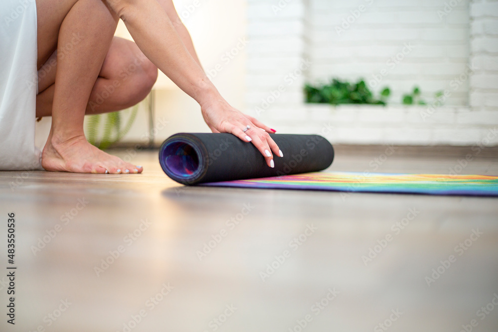 Naklejka premium Close-up of a woman's hands rolling up an exercise mat and getting ready for a yoga class. With copyspace for text or logo