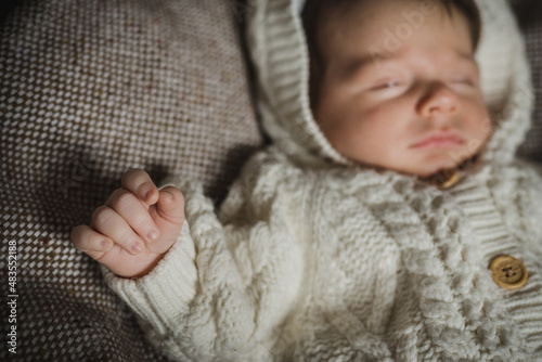 Fotografie A portrait of little newborn in white cozy knitted overall laying on beige woollen plaid