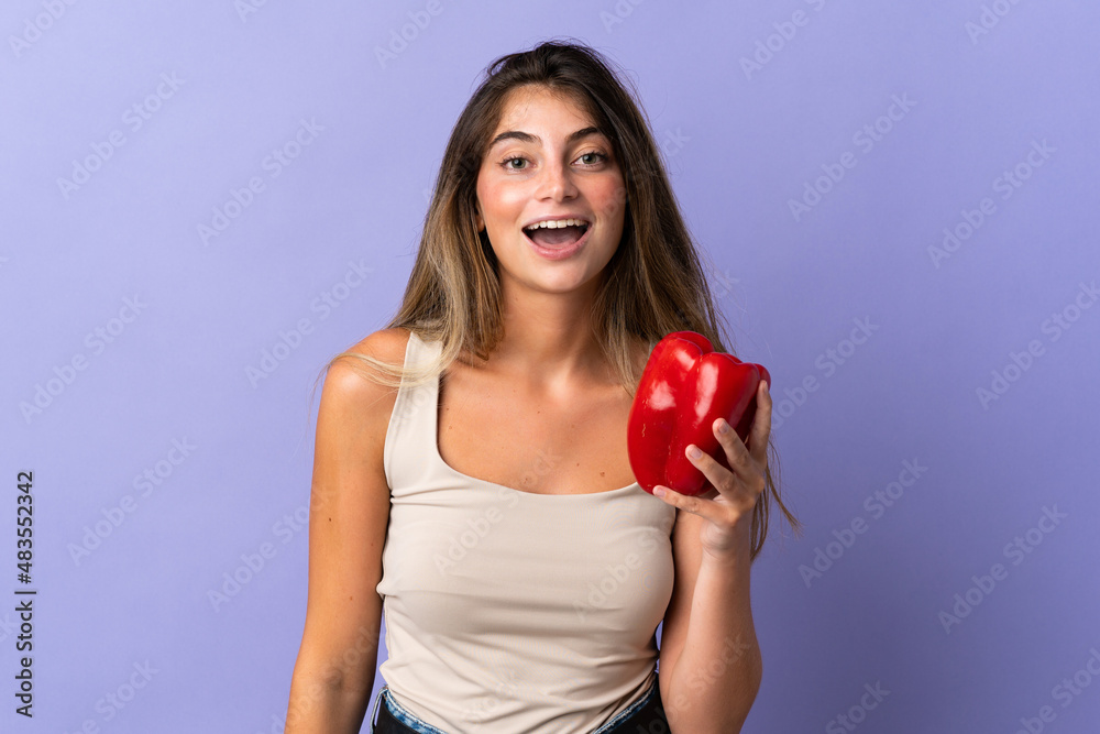 Young woman holding a pepper isolated on purple background with surprise and shocked facial expression Young woman holding a pepper isolated on purple background with surprise and shocked facial expression