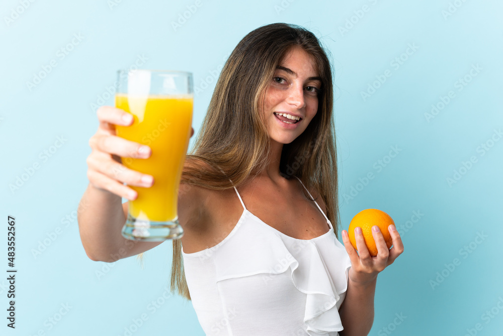 Young caucasian woman isolated on blue background holding an orange and an orange juice Young caucasian woman isolated on blue background holding an orange and an orange juice