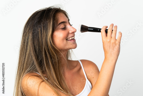 Young caucasian woman isolated on white background holding makeup brush and whit happy expression
