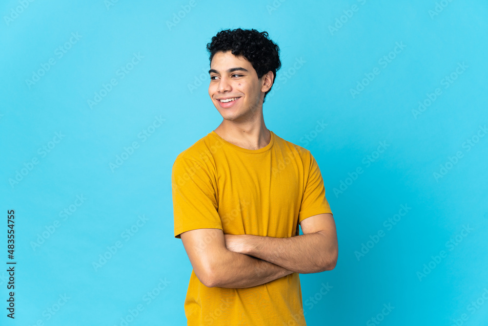 Young Venezuelan man isolated on blue background with arms crossed and happy Young Venezuelan man isolated on blue background with arms crossed and happy