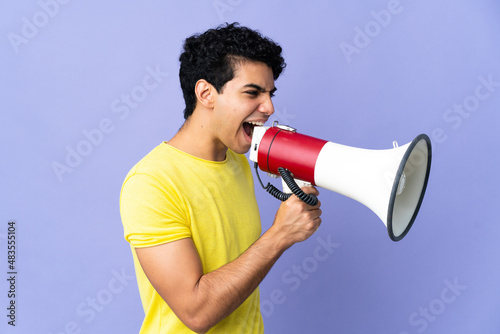 Young Venezuelan man isolated on purple background shouting through a megaphone to announce something in lateral position