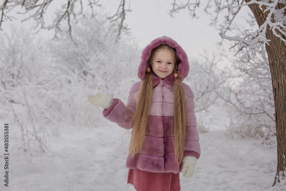 a blonde girl in a pink fur coat plays in a snowy winter forest a blonde girl in a pink fur coat plays in a snowy winter forest