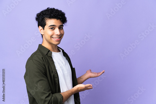 Young Venezuelan man isolated on purple background extending hands to the side for inviting to come