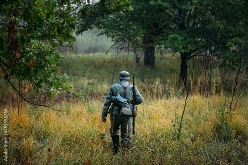 Single Re-enactor Dressed As German Wehrmacht Infantry Soldier In World War II Walking In Patrol Through Autumn Forest. WWII WW2 Times.