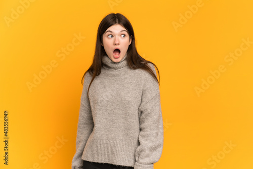 Young Ukrainian girl isolated on yellow background doing surprise gesture while looking to the side © luismolinero