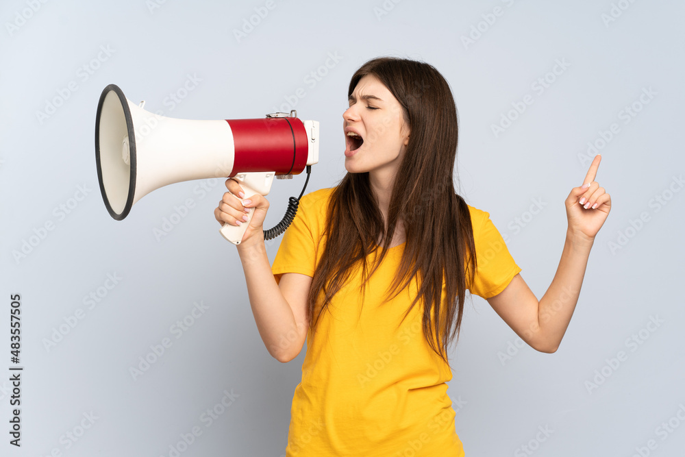 Naklejka premium Young Ukrainian girl isolated on white background shouting through a megaphone to announce something in lateral position