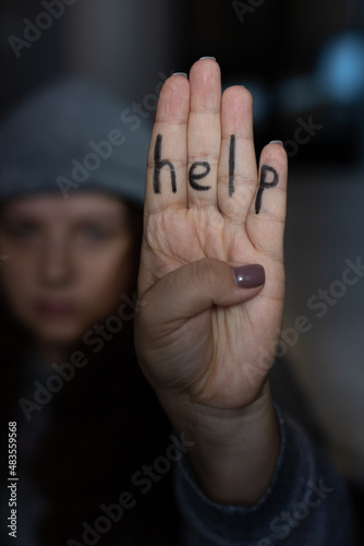 Young woman wearing gray hat showing four fingers with inscription on hand saying help. Sign of domestic violence. Physical, mental, psychological abuse. Victim of beating and under pressure. 