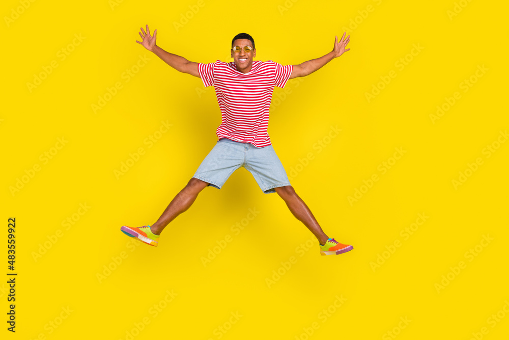 Full length photo of youth guy jump hold hands aside wear red striped outfit isolated over bright yellow color background