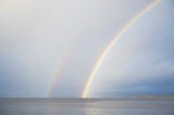 Bright rainbow high in sky over sea during dark storm