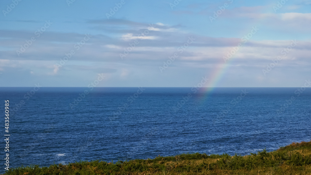 rainbow disappearing into the wild blue ocean