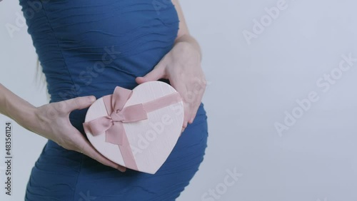 a pregnant woman in a blue dress twirls a pink heart-shaped box with a bow on her stomach. a gift for Valentine's Day or March 8th. video in slow motion.