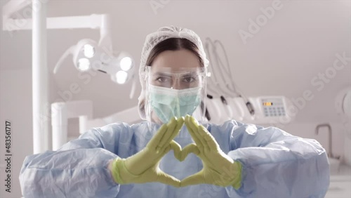 Female surgeon in dental office shows a heart with her hands and smile. High quality 4k footage. concept dentist