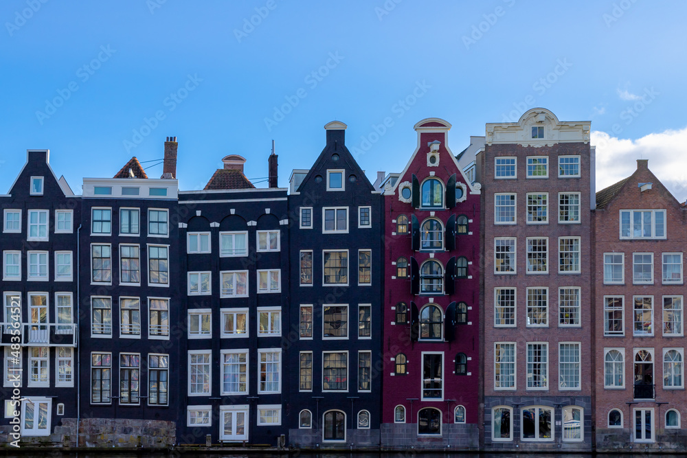 Architecture features traditional houses with blue sky, Typical dutch house at Damrak canal, An avenue running between Amsterdam Centraal in the north and Dam Square in the south, Holland, Netherlands