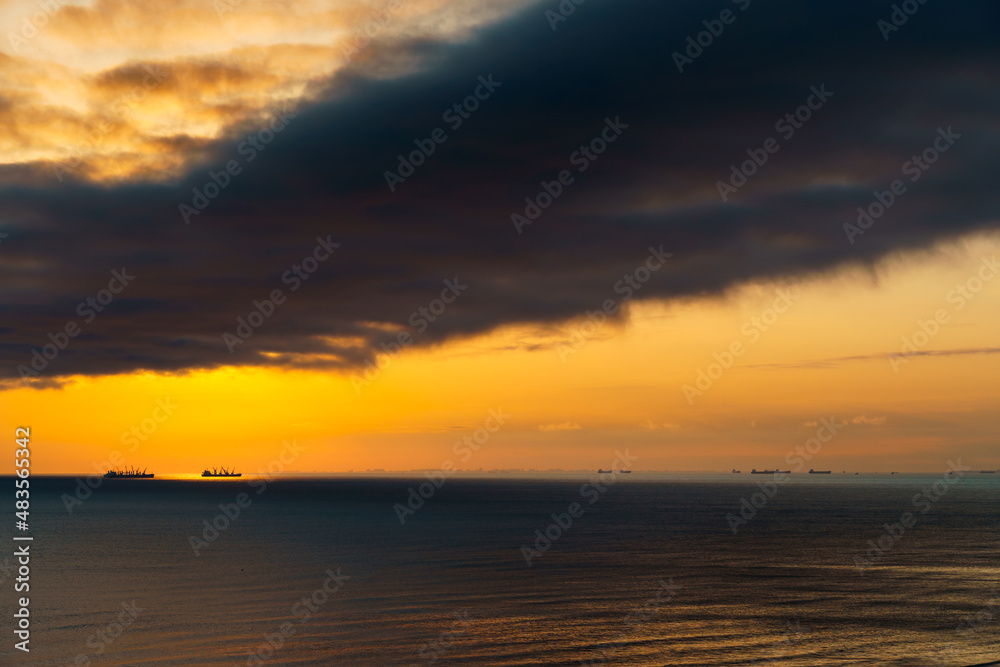 silhouettes of ships at sea, dramatic seascape with sunset sky, sunlight reflected from the waves