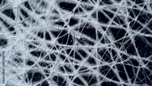 Girl and guy tourists are posing on the frozen lake Baikal lying down. Shooting from a drone