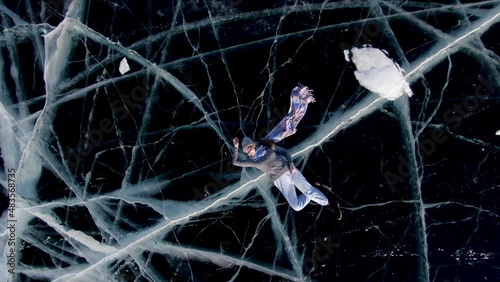 Girl and guy tourists are posing on the frozen lake Baikal lying down. Shooting from a drone