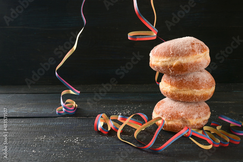 Stacked Berliner doughnuts or Krapfen and some party streamers against a dark rustic background, often served on New Year and carnival, copy space, selected focus
