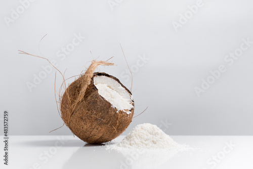 Coco abierto con hojuelas de coco ralladas que se derraman sobre una mesa blanca	 photo