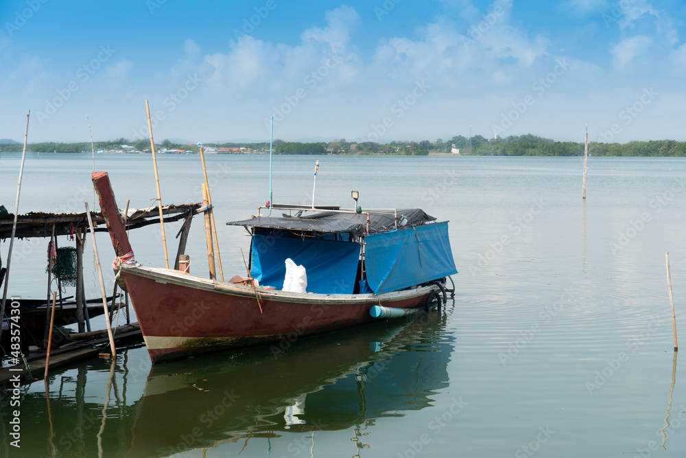 Small fishing boats docked on the vast river in Thailand. And the background image of the forest and small communities along the river under blue sky.
