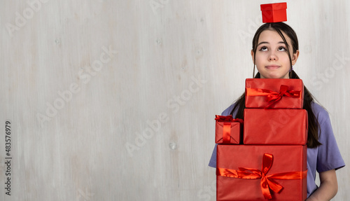 A happy teenage girl holds a lot of boxes with gifts in her hands. Red gift box with ribbon.