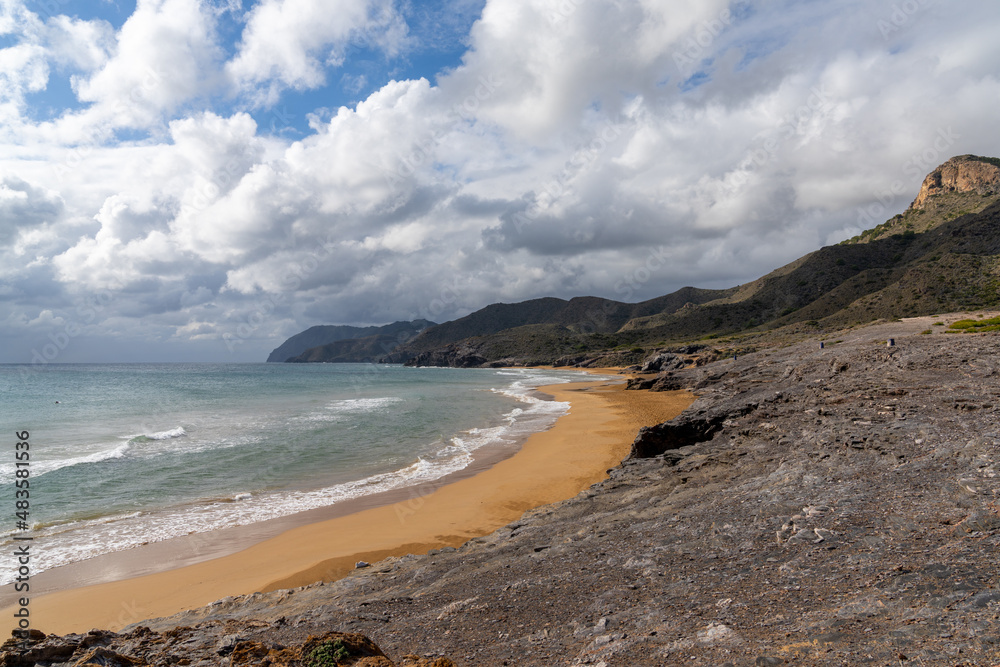 rocky ocean coast with mountains and a beautiful golden sand beach in the foreground