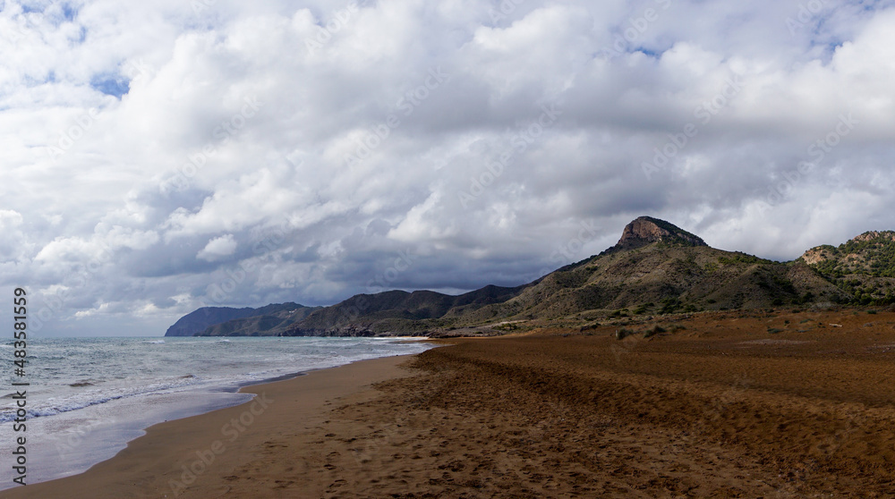 golden brown sandy beach landscape with mountain landscape behind under an expressive sky