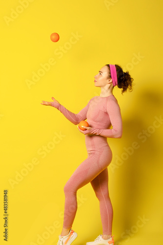 Athletic beautiful girl holding oranges on yellow background