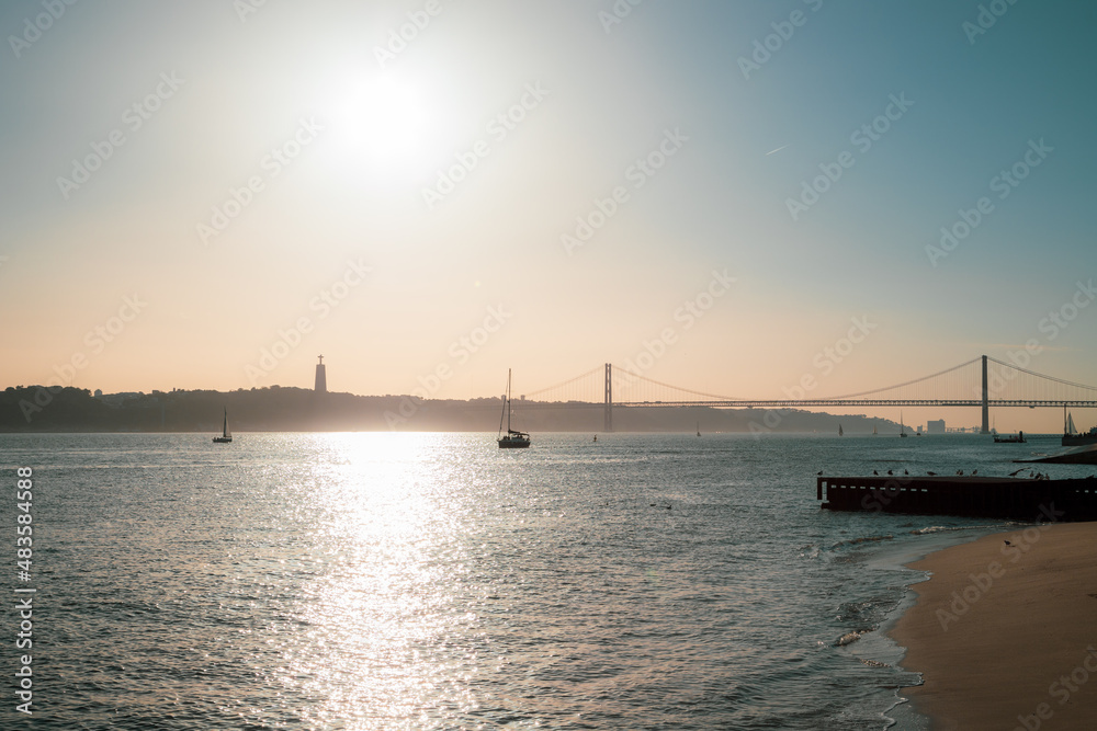 Sunset seen at Terreiro do Paço with 25 april bridge and sailboats on the River