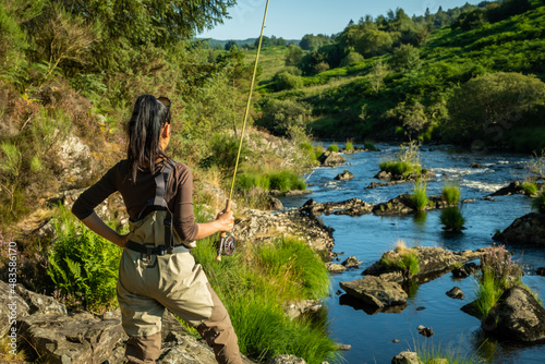 An asian female fly fisher women wearing waders and holding a rod