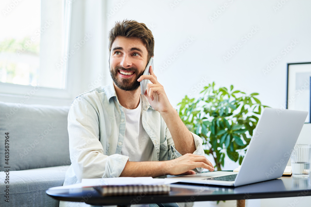 Happy young freelancer talking on the phone working from home on laptop Happy young freelancer talking on the phone working from home on laptop