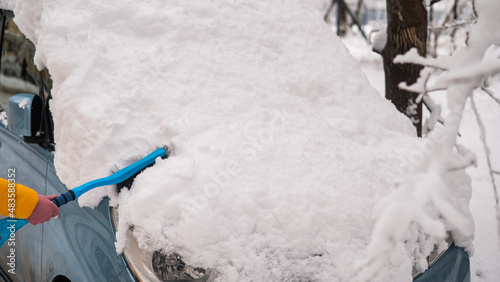 Caucasian woman brushing a car from freshly fallen snow. 