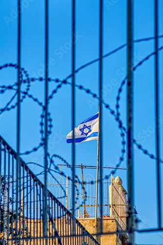 waving flag of the state of israel behind barbed wire on a sunny day