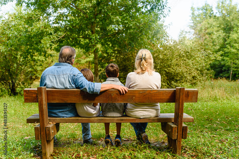 Children and grandparents sit together on wood bench in the park Children and grandparents sit together on wood bench in the park
