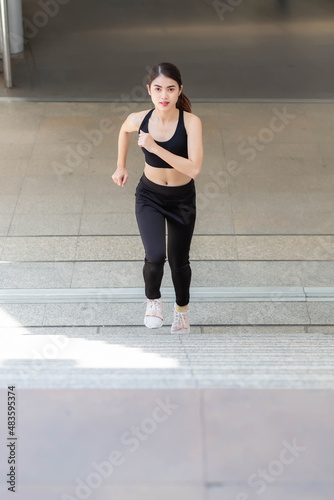 A Thai Southeast Asian woman in black workout clothes running up the stairs.