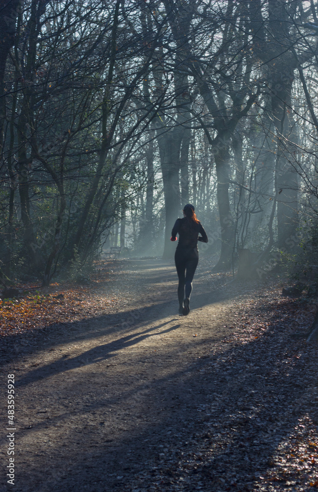 Woman with red hair running through sunlit woods.