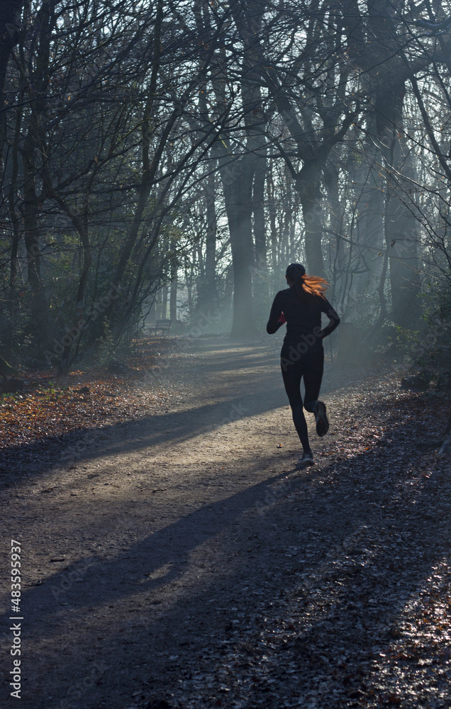 Woman with red hair running through sunlit woods.