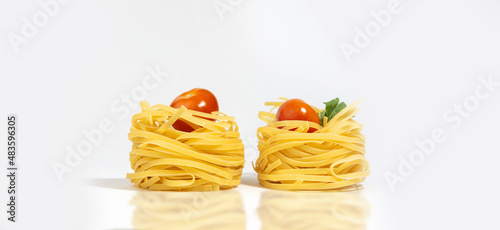 Italian pasta. Spaghetti Capellini, with cherry tomatoes and greens, isolated on a white gray background with hard shadows and reflection. Pasta in the form of nests. Creative photo of pasta. Banner