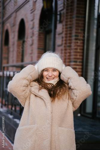 A young woman smiles beautifully and straightens her hat with her hands, winter