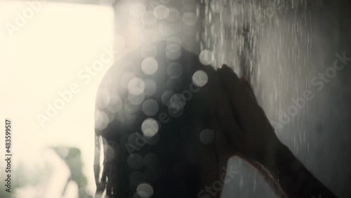 Black haired woman taking a shower and washing her face and hair while the condensation drops in front of the shower cubicle find their way down. Close up shot photo