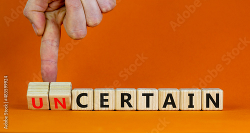 Certain or uncertain symbol. Businessman turns wooden cubes and changes the concept word uncertain to certain. Beautiful orange background, copy space. Business certain or uncertain concept.