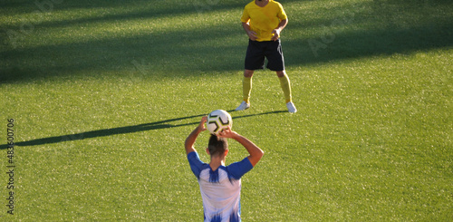 Jogo de futebol com um jogador de equipamento azul e branco a lançar a bola para dentro do campo - adversário de equipamento amarelo e branco - lance de lançamento photo