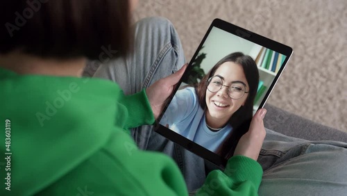 Happy funny caucasian teenager sitting on couch at home, waving hand, showing thumbs up, on tablet and chatting cheerfully on video call with her girl friend, sister, mother, teacher. 4k footage