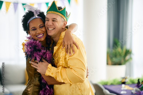 Happy man and his African American friend in Mardi Gras costumes have fun and embrace on a party.