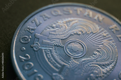 Translation: Kazakhstan. Kazakh 50 tenge coin with the country emblem and focus on shanyrak. Close-up. Blue tinted background or wallpaper for Kazakh economy or state. Macro