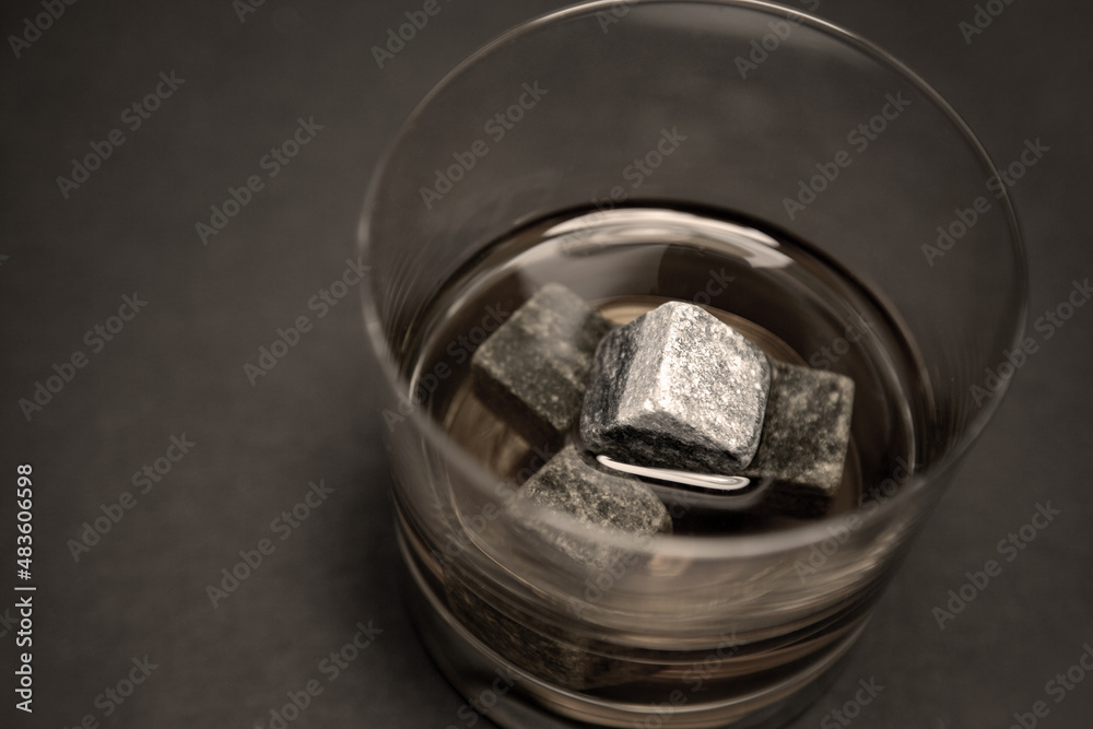Gray whiskey soapstonestones in the glass. Close up view of whisky stones in the glass with whisky isolated on dark background whith copyspace