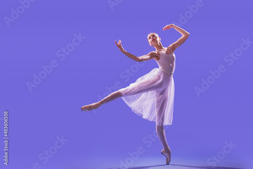 an elegant ballerina in pointe shoes is dancing in a long flying white skirt on a lilac light background